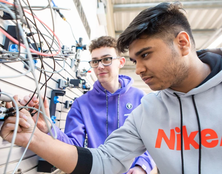 Two students working together on a pneumatics system, connecting wires and tubes to an industrial training panel. Two students working together on a pneumatics system, connecting wires and tubes to an industrial training panel.